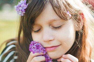 Portrait. A cute dark-haired girl with a lilac branch in her hands. She closed her eyes and smelled the flowers. Close-up. High quality photo. Copyspace 