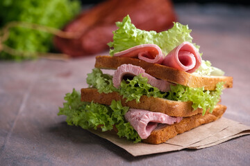 Big sandwich witn green leaves and beef on wooden board, black background