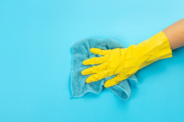 worker hand in a yellow rubber protective glove with micro fiber blue cloth wiping a blue wall from...