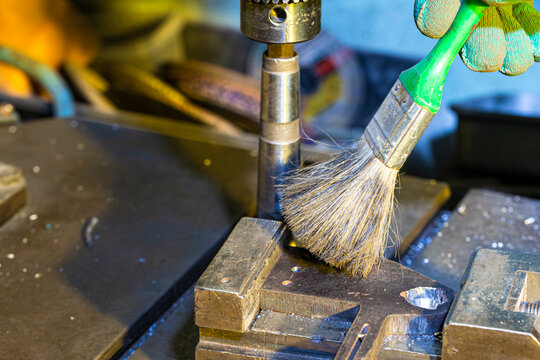 Metal Processing. Fitter Man Using Special Brush for Cleaning Metal Drilling Machine From Metal Shavings in Workshop.