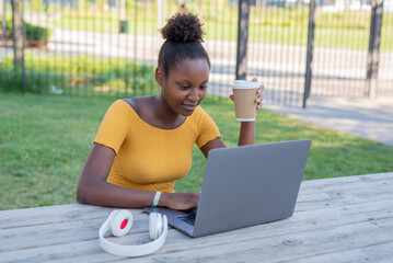 young african fashion woman studying outdoors, blogger working in the city while drinking takeaway...