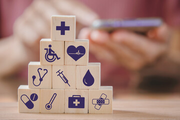 health and medical icon on stack of wooden coins and blurred people holding smartphone for health insurance, wellness, wellbeing concept