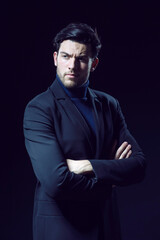 Portrait of Serious Handsome Caucasian Brunet Businessman Wearing Black Suit Posing With Folded Hands Looking Aside Against Black Studio Background.