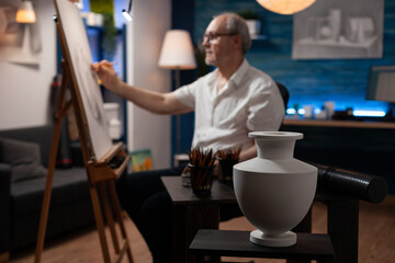 White model vase on wooden table used for light study by retired man artist drawing using sharp...