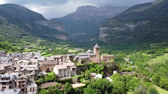 Torla, Ordesa Valley, Huesca, Pyrenees, Spain - Aerial Drone View (Pan Up) of the Church, Green Valley, Blue River and Dark Mysterious Mountains