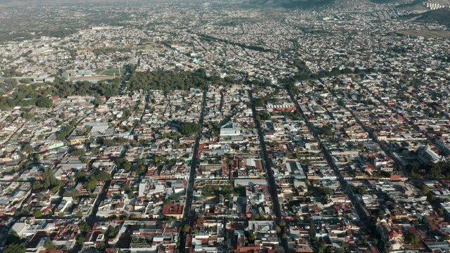 Huge long linear walking streets with many housing blocks and green trees in the large city of Oaxaca with the great mountains of southern Sierra Madre in the background. Drone tilt shot