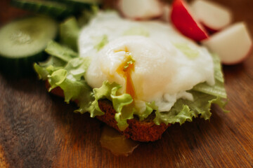 Poached egg on toast with herbs and vegetables on a wooden background