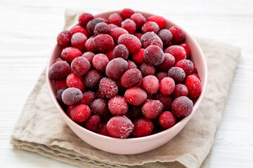 Frozen Cranberries in a Pink Bowl on a white wooden background, low angle view.