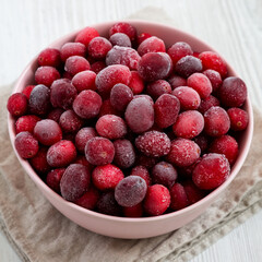 Frozen Cranberries in a Pink Bowl on a white wooden background, side view. Close-up.