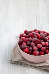 Frozen Cranberries in a Pink Bowl on a white wooden surface, side view. Copy space.
