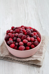 Frozen Cranberries in a Pink Bowl on a white wooden surface, side view. Space for text.