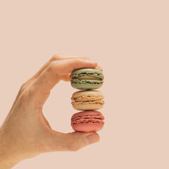 The man's hand holding green, beige and pink color attractive and yummy macaron . Champagne background.