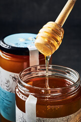 Wooden honey dipper spoon taking honey from jar.