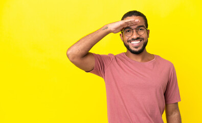 Fototapeta na wymiar Young latin man isolated on yellow background saluting with hand with happy expression