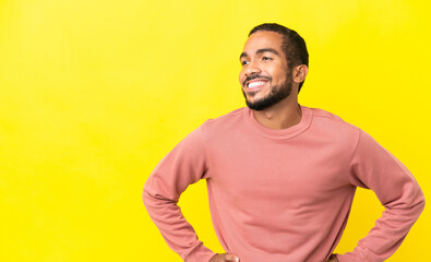 Young latin man isolated on yellow background posing with arms at hip and smiling