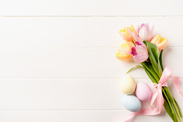 easter background with eggs and tulips on white wooden backdrop, top view flat lay