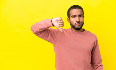 Young latin man isolated on yellow background showing thumb down with negative expression