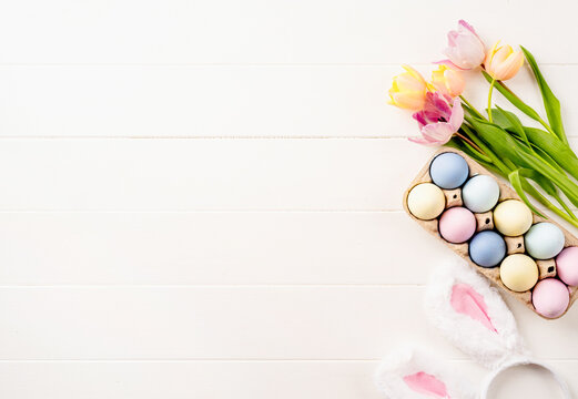 easter background with eggs, tulips and bunny ears on white wooden backdrop, top view flat lay
