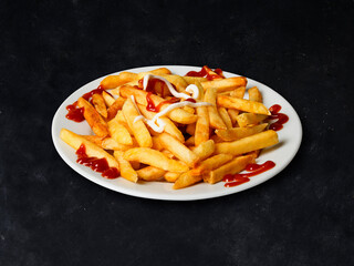Homemade french fries with Ketchup, Salt and Pepper on a white plate on a black background, top view.