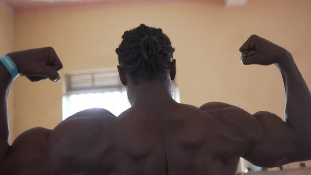 Black African bodybuilder posing in an old school gym in Africa. Back classic bodybuilding pose fitness motivation concept in a poor countries of Africa 4K.