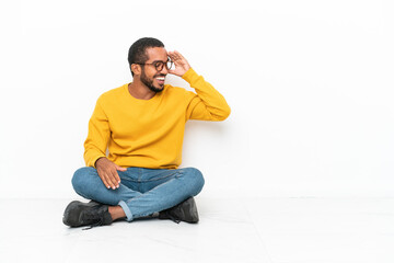 Young Ecuadorian man sitting on the floor isolated on white wall laughing