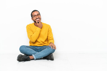 Young Ecuadorian man sitting on the floor isolated on white wall smiling