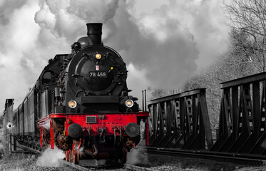 Fototapeta na wymiar Steam train with historic locomotive passing a steel construction bridge spanning over Ruhr river near Arnsberg Sauerland Germany on Ruhr Valley line. Vintage greyscale railway with colored engine.