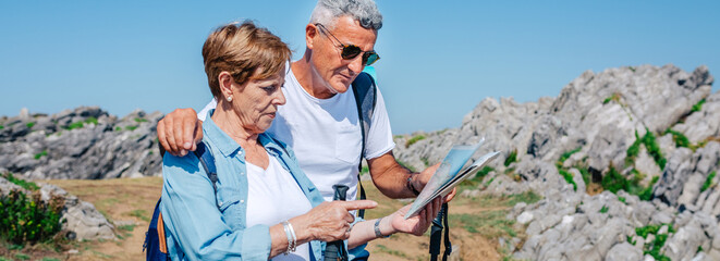 Senior couple with poles hiking looking map outdoors