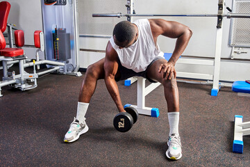 Fototapeta na wymiar An African American man shakes his biceps while sitting on a bench in the gym