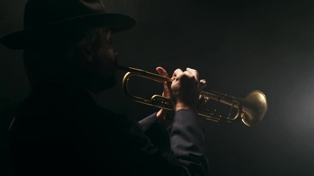 Professional male musician plays musical trumpet, pressing valves in studio on black background with smoke, back view. Concept of jazz music and blues