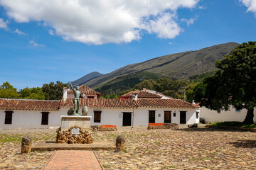 Fototapeta na wymiar Monument and traditional buildings at Plaza Mayor of Villa de Leyva, Colombia, blue sky, white clouds and mountains in background 