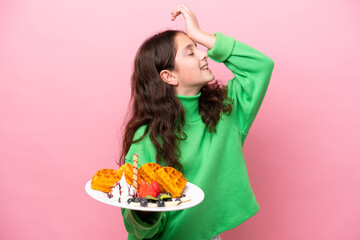 Little caucasian girl holding waffles isolated on pink background has realized something and intending the solution