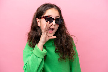 Fototapeta premium Little caucasian girl wearing sunglasses isolated on pink background shouting with mouth wide open