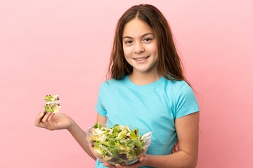 Little caucasian girl isolated on pink background holding a bowl of salad with happy expression