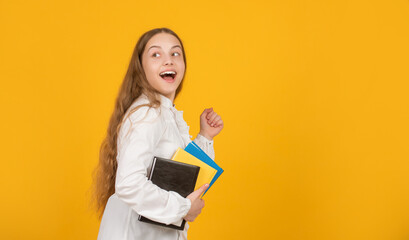 surprised happy running kid with school homework on yellow background with copy space, childhood