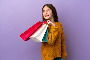 Little caucasian girl isolated on purple background holding shopping bags and smiling