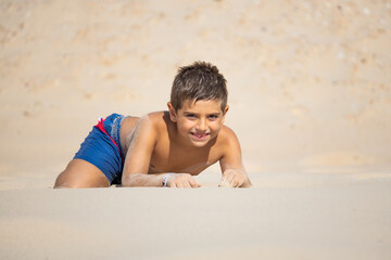 Funny kid lying down on a sand of a beach