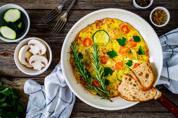 Breakfast - omelette with bacon, bread and vegetables in frying pan
