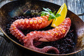 Cooked octopus and black rice in frying pan on wooden table

