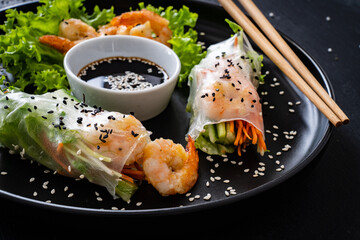 Rice and tapioca paper rolls with prawns and fresh vegetables on wooden black table
