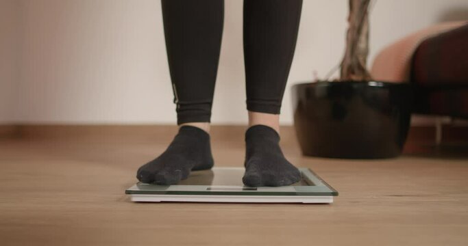 Woman in socks stepping on scale to see her weight. Girl wants to know if she lost weight and is getting on a scale