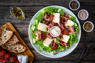 Tasty salad - prosciutto di Parma, camembert and fresh, green vegetables on wooden table
