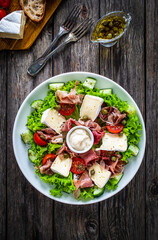 Tasty salad - prosciutto di Parma, camembert and fresh, green vegetables on wooden table
