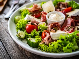 Fotobehang Tasty salad - prosciutto di Parma, camembert and fresh, green vegetables on wooden table  © Jacek Chabraszewski