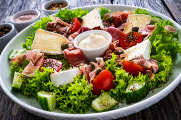 Tasty salad - prosciutto di Parma, camembert and fresh, green vegetables on wooden table
