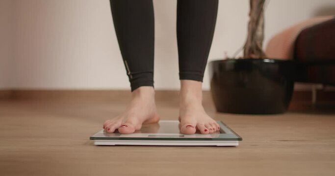 Woman stepping on and off scale. Girl wiggling with foot toes while standing on scale checking her weight after workout.