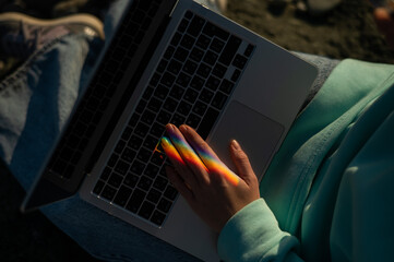A woman is typing on a laptop. Rainbow light from a prism. 