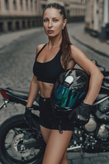 Attractive woman motorcyclist and her black bike in alley