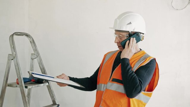 Foreman calls the customer, discusses the estimate for the project. Foreman in protective safety vest, goggles and hard hat call the customer on phone to make changes in construction plan.