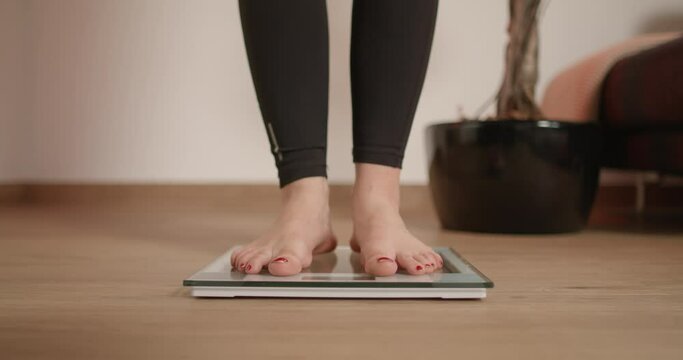 Young woman stepping on scale and wiggling her toes while checking her weight after workout and fitness